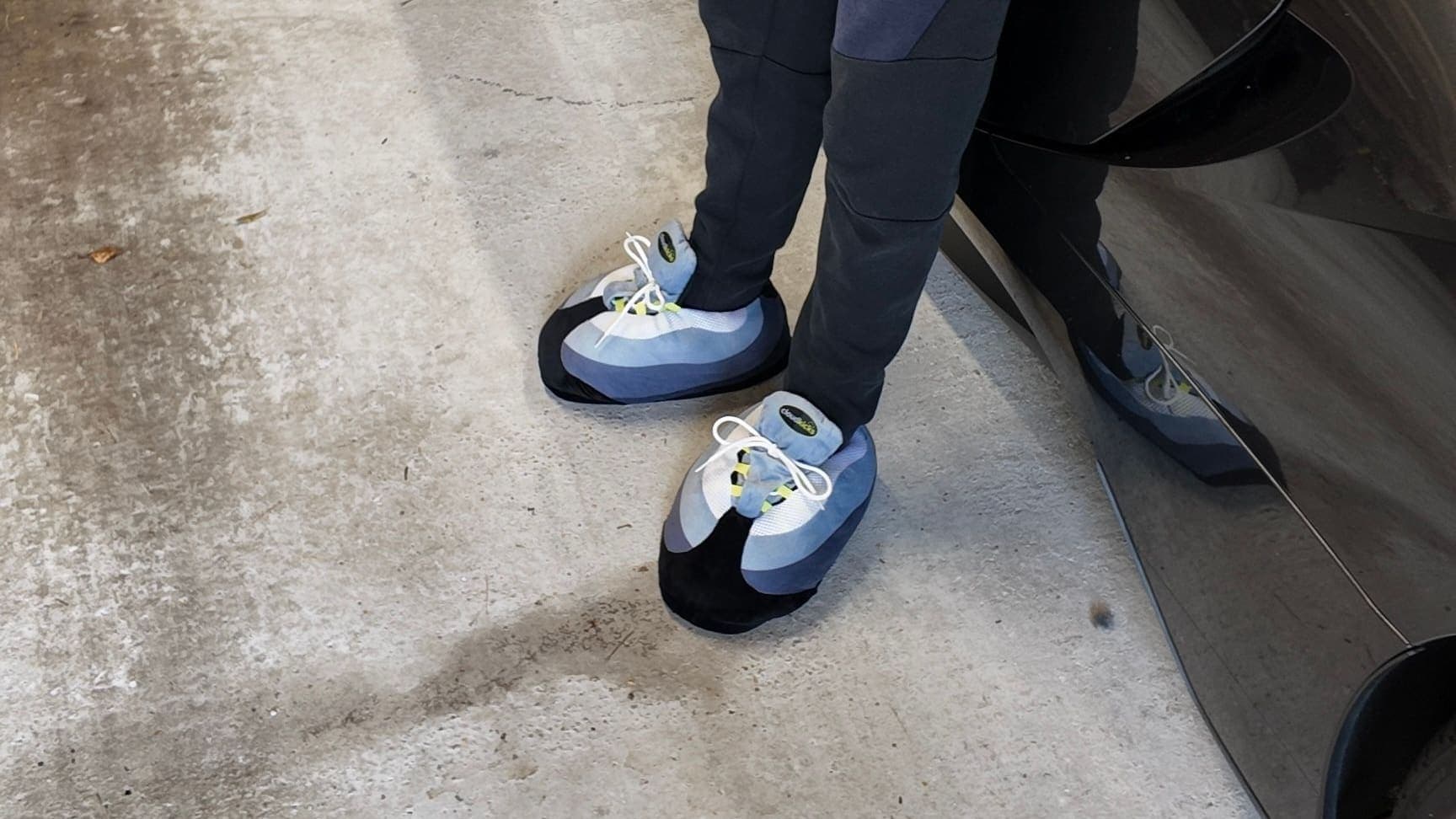 Arms crossed, leaning on a black sports car in OG Neon CloudKicks