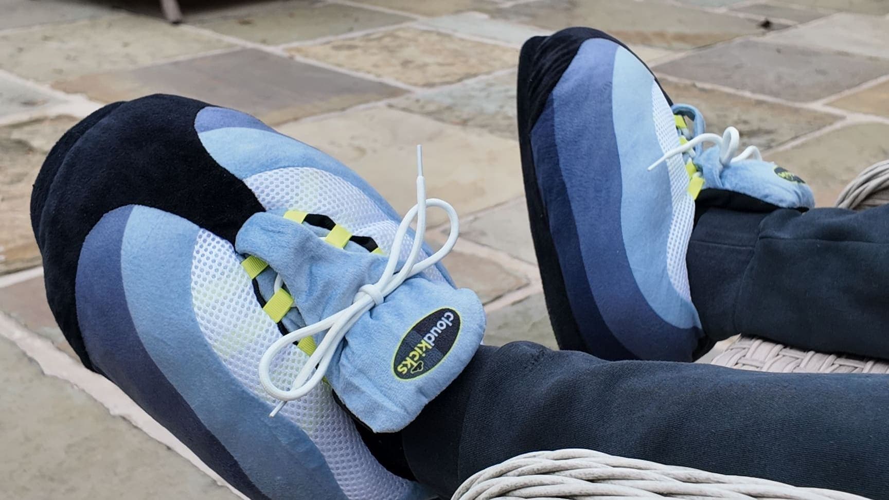 Feet up in OG Neon CloudKicks on rattan furniture, stone patio below