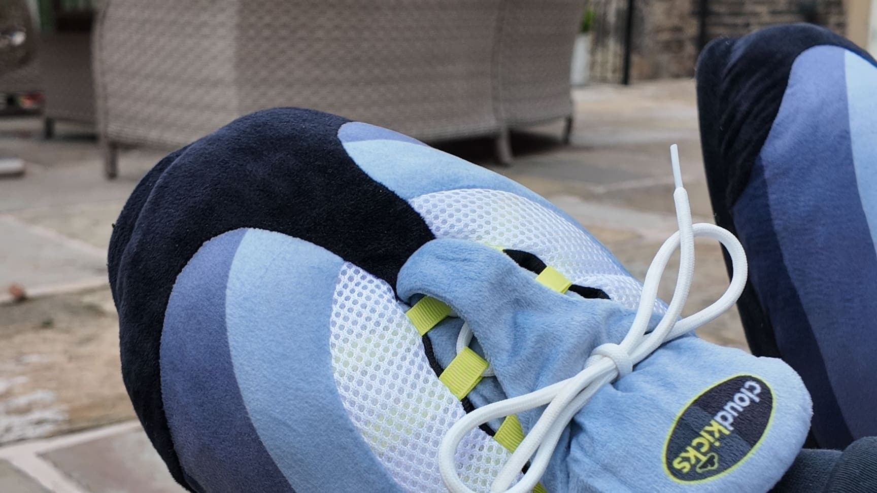 Close-up of OG Neon CloudKicks with feet up on the patio, rattan chairs behind
