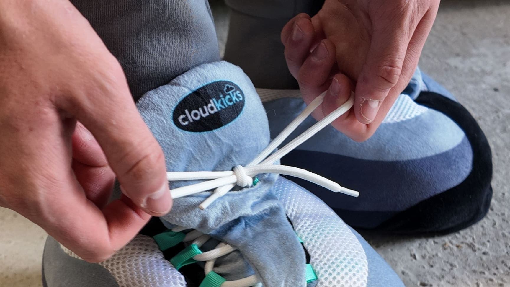 Hands lacing up a Hyper Turquoise CloudKick on a concrete floor