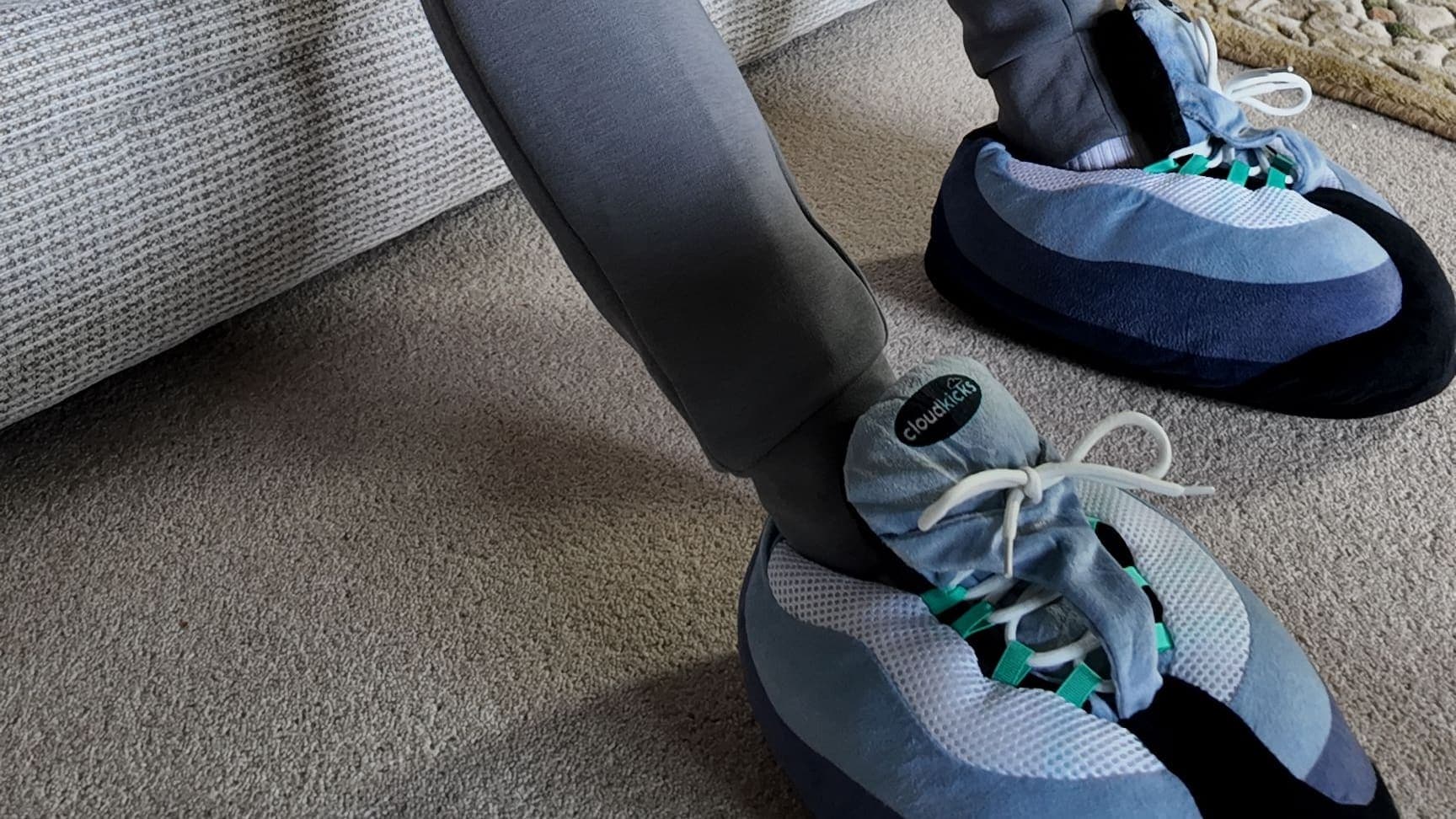 Grey joggers and Hyper Turquoise CloudKicks on the carpet beside a cream sofa