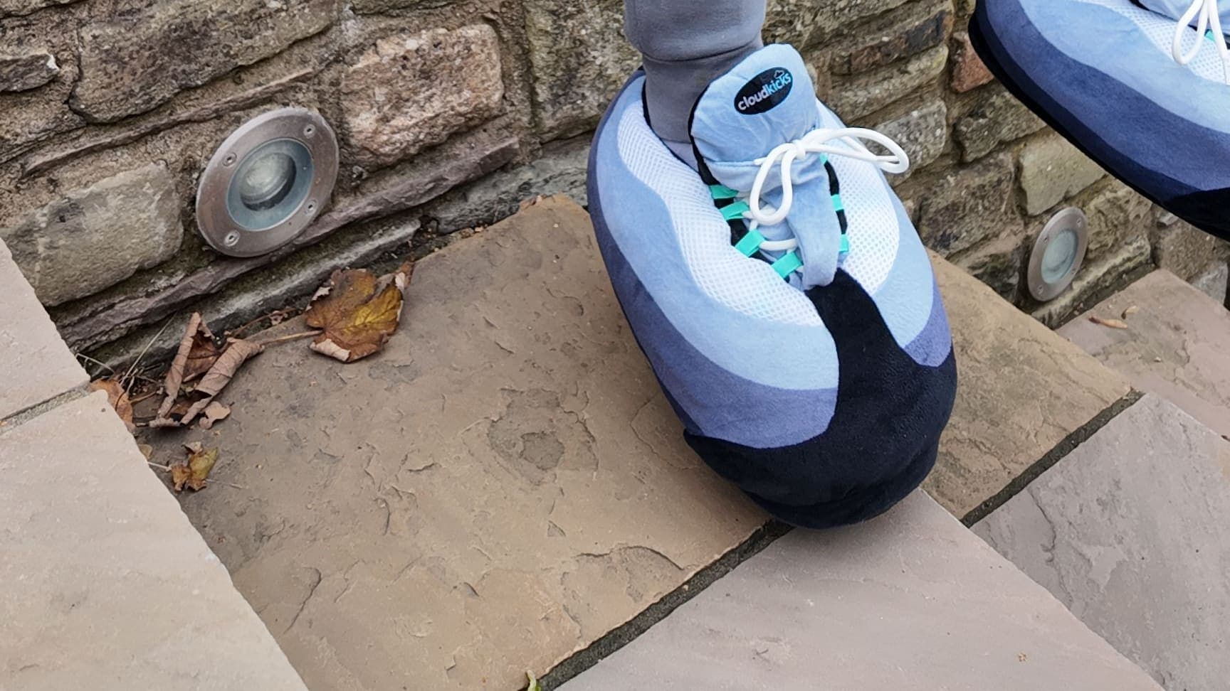 A Hyper Turquoise CloudKick on a stone step, grey joggers above and an old stone wall behind